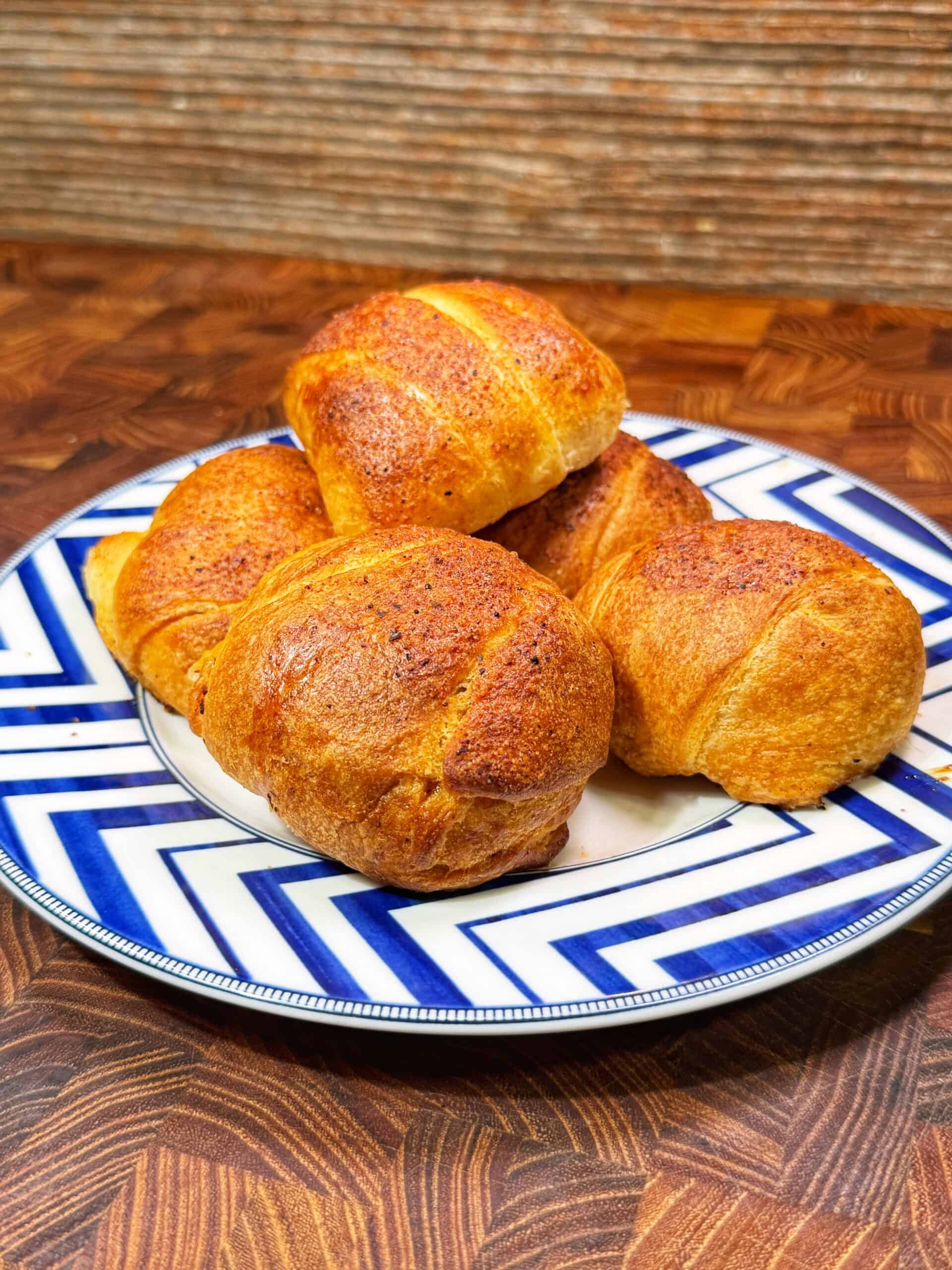 A blue and white patterned plate holds four golden-brown, freshly baked pulled pork bombs on a wooden surface with a textured brown background.