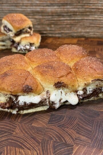 A close-up of sweet pull-apart rolls filled with melted chocolate and gooey marshmallow on a wooden surface, with some buns separated in the background.