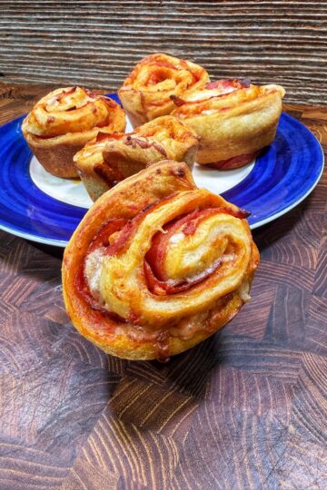 Four pizza rolls with visible layers of dough, cheese, and tomato sauce, are arranged on a blue plate, with one roll in the foreground on a wooden surface, and a rustic wood background behind them.