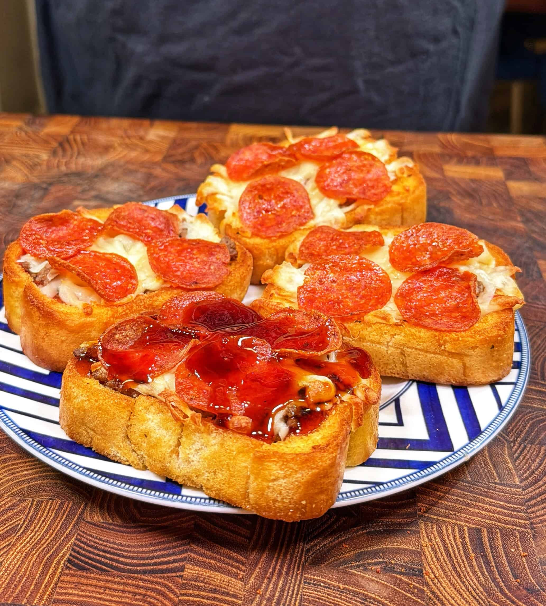 Three slices of thick bread topped with melted cheese and pepperoni are arranged on a decorative plate, with one slice featuring a glossy, reddish sauce. The plate sits on a wooden surface.