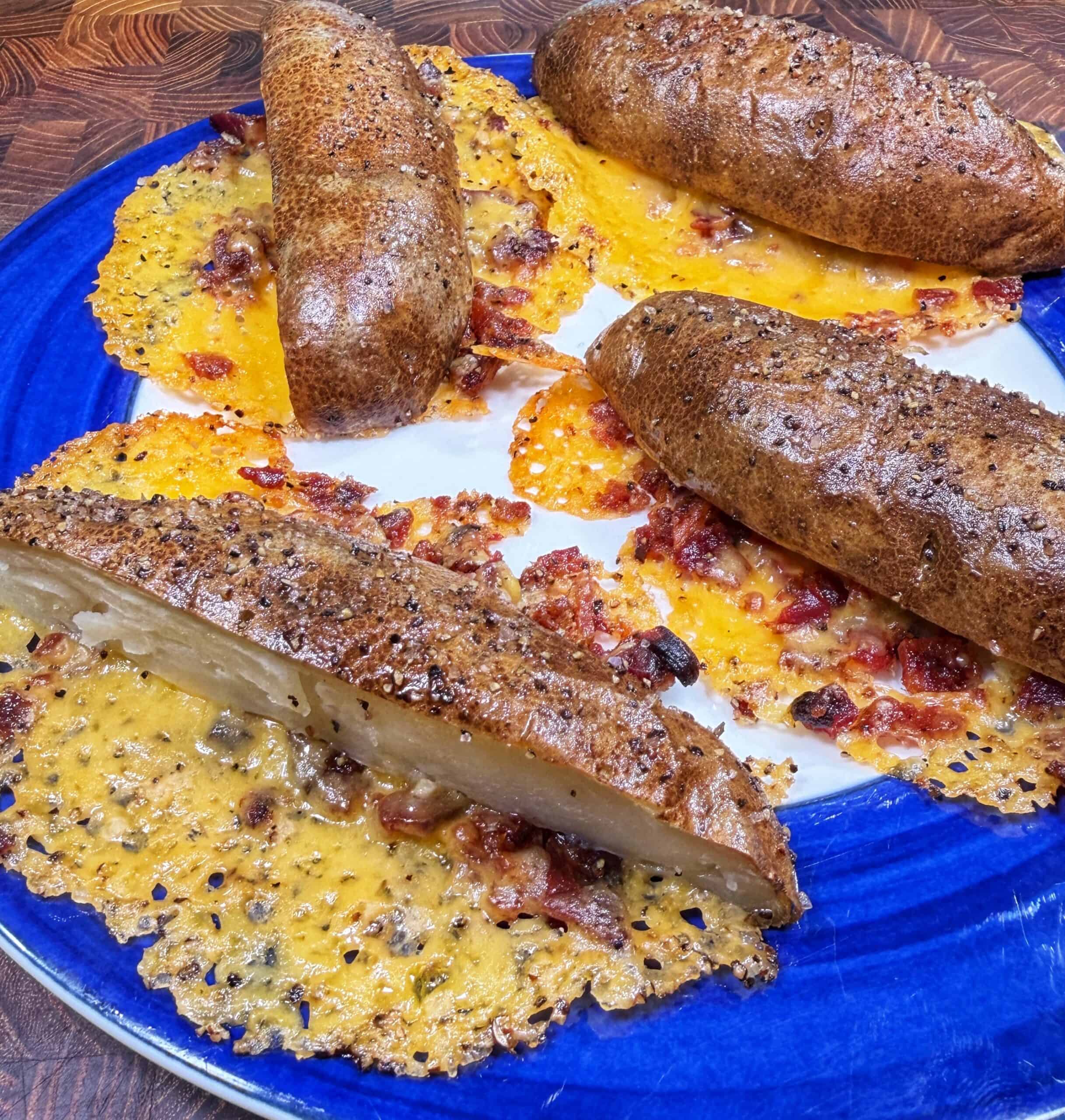 Four baked potatoes and one baked potato half are on a blue plate, surrounded by crispy melted cheese and bacon that has spread out onto the plate and hardened into a lacy, golden layer.