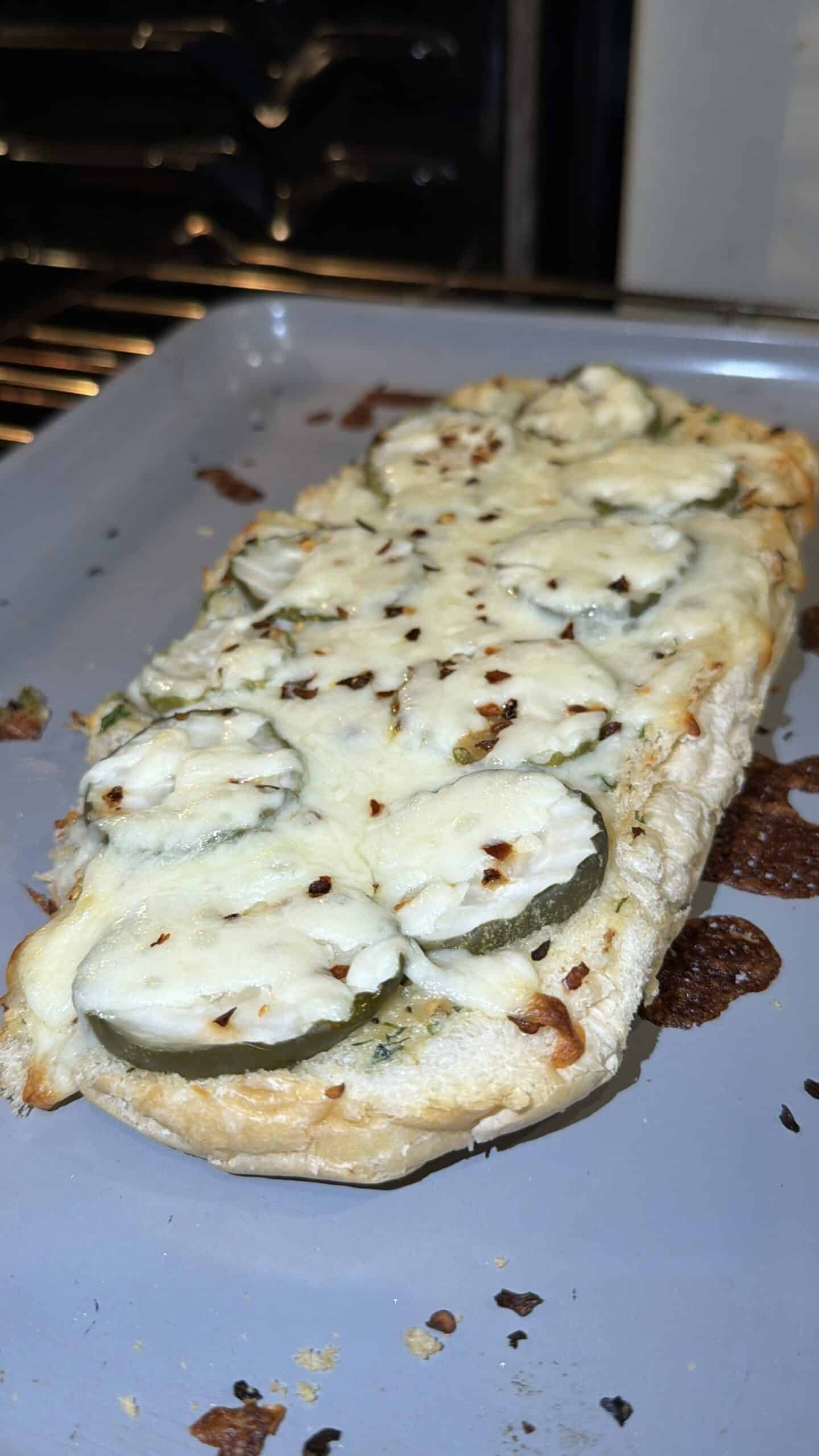 A toasted flatbread topped with melted cheese, zucchini slices, and red pepper flakes sits on a baking tray, fresh out of the oven.