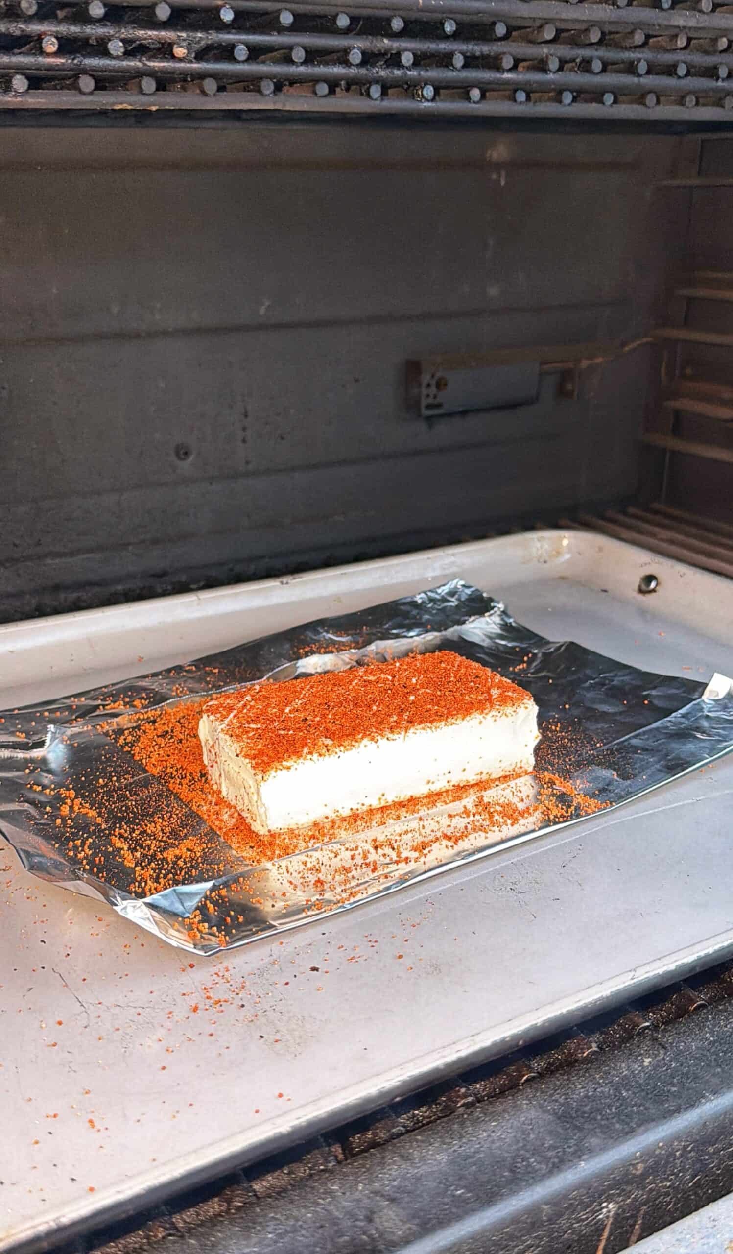 A rectangular block of cheese sprinkled with red seasoning sits on a sheet of <a href=