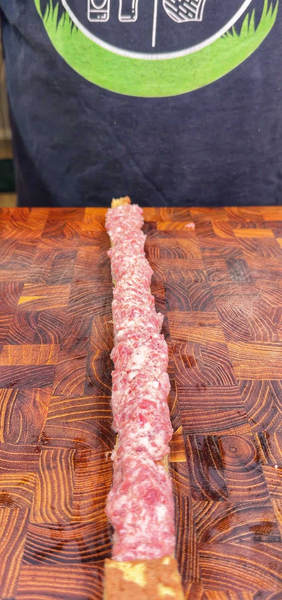 A close-up of a raw minced meat skewer placed on a wooden <a href=