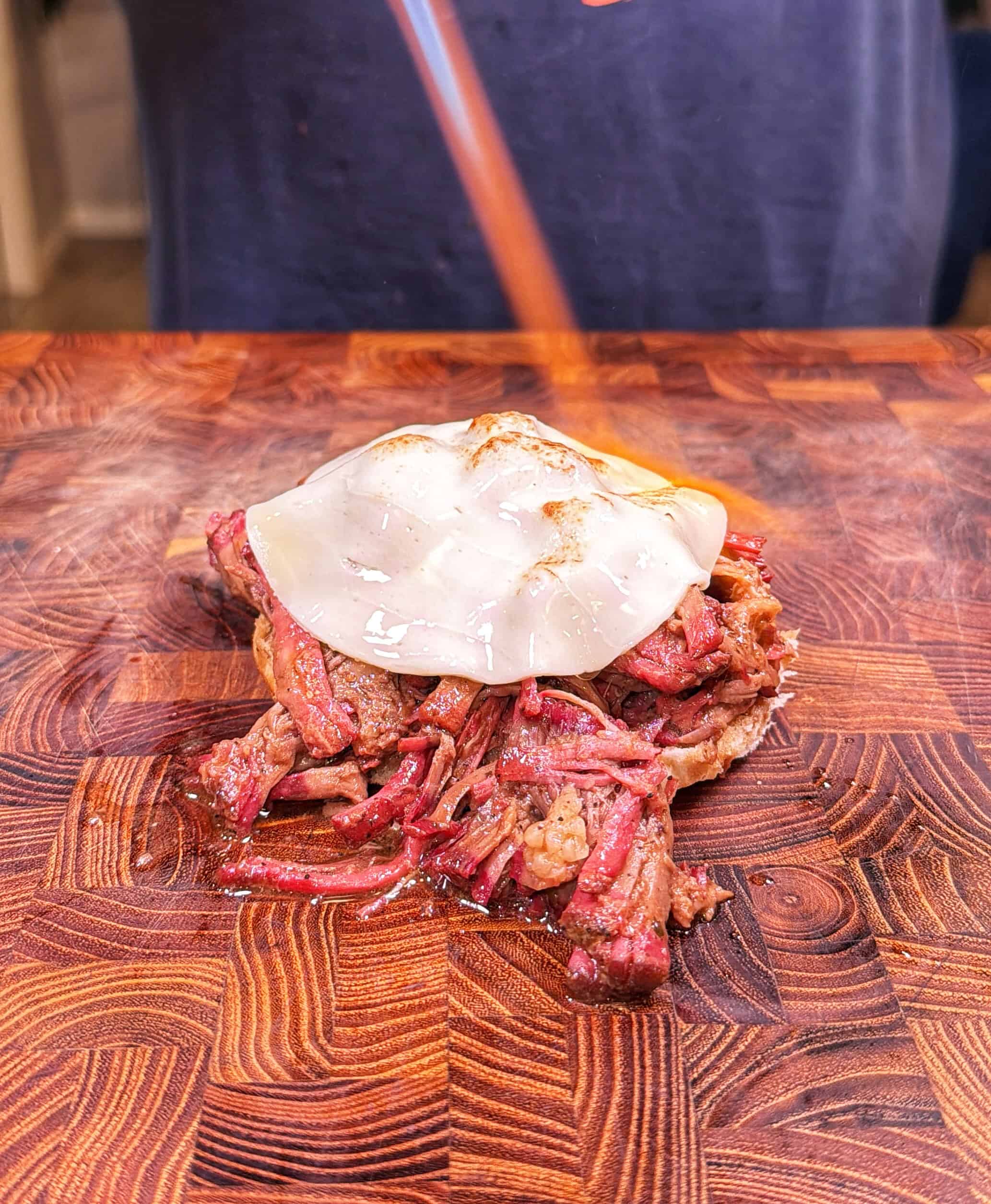 Melted cheese is being torched on top of a pile of shredded meat on a wooden <a href=