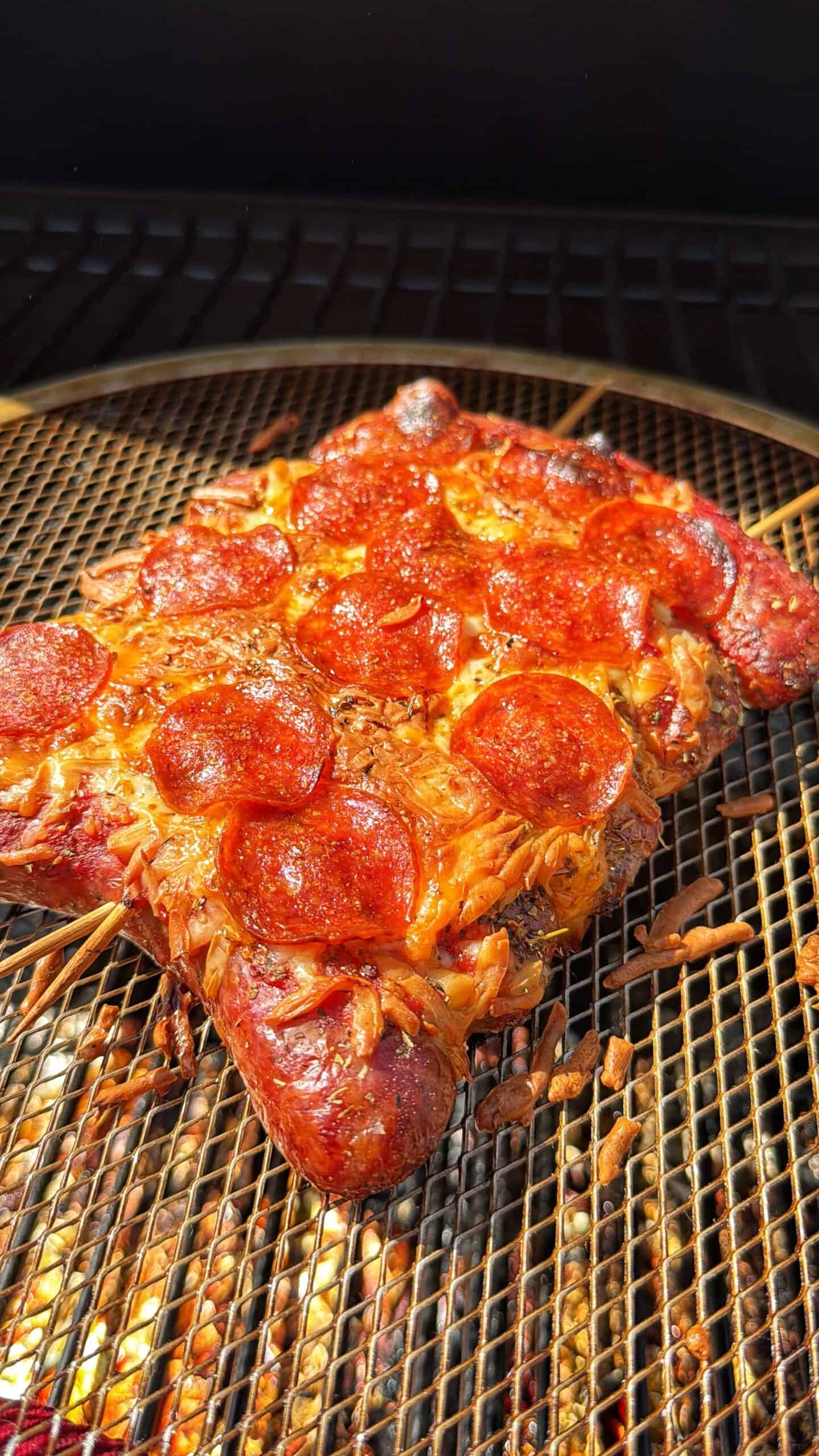 A smoked meat dish shaped like a turtle, covered with melted cheese and pepperoni slices, is cooking on a grill rack above <a href=