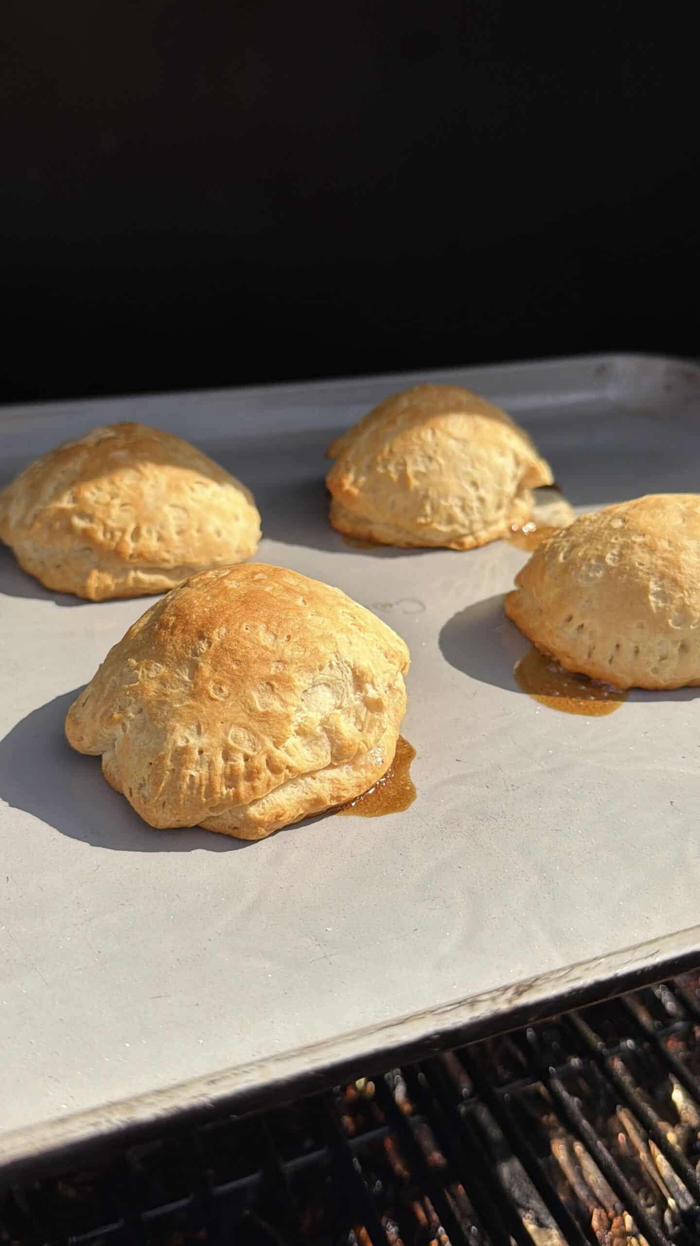 Four golden-brown hand pies with filling oozing out slightly are baking on a parchment-lined <a href=