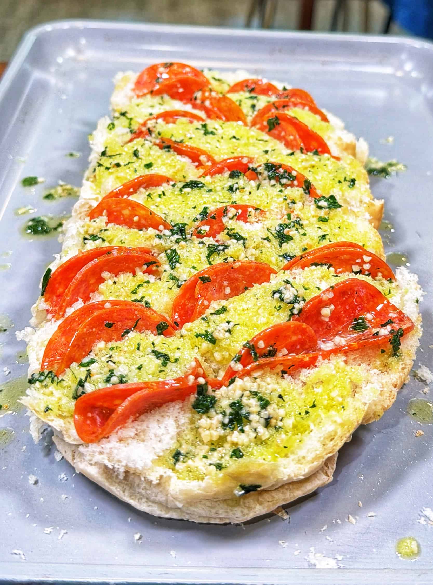 Sliced bread topped with tomato slices, shredded cheese, herbs, and a drizzle of olive oil, arranged neatly on a baking tray, ready to be baked.
