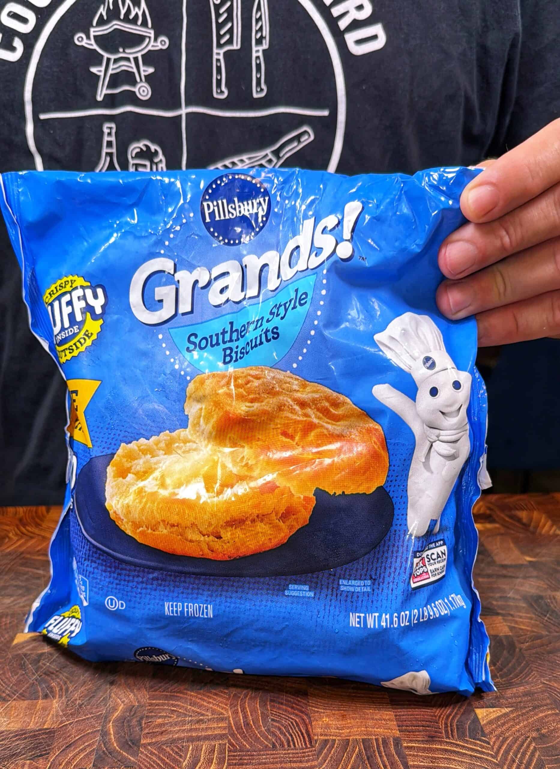A person holds a bag of Pillsbury Grands! Southern-style biscuits featuring a biscuit image and the Pillsbury Doughboy on the blue packaging.