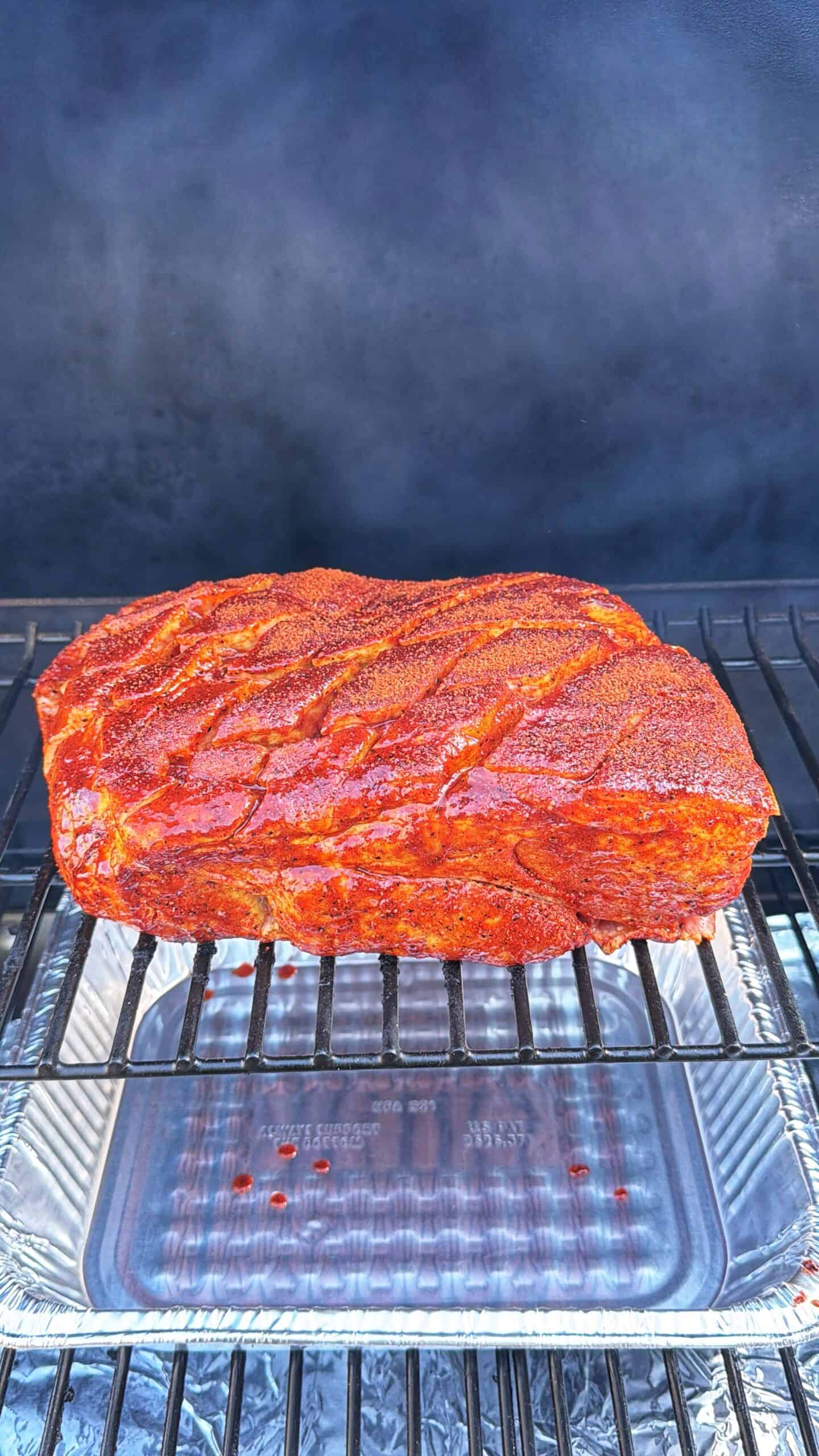 A large, seasoned piece of meat sits on a grill rack over a foil <a href=