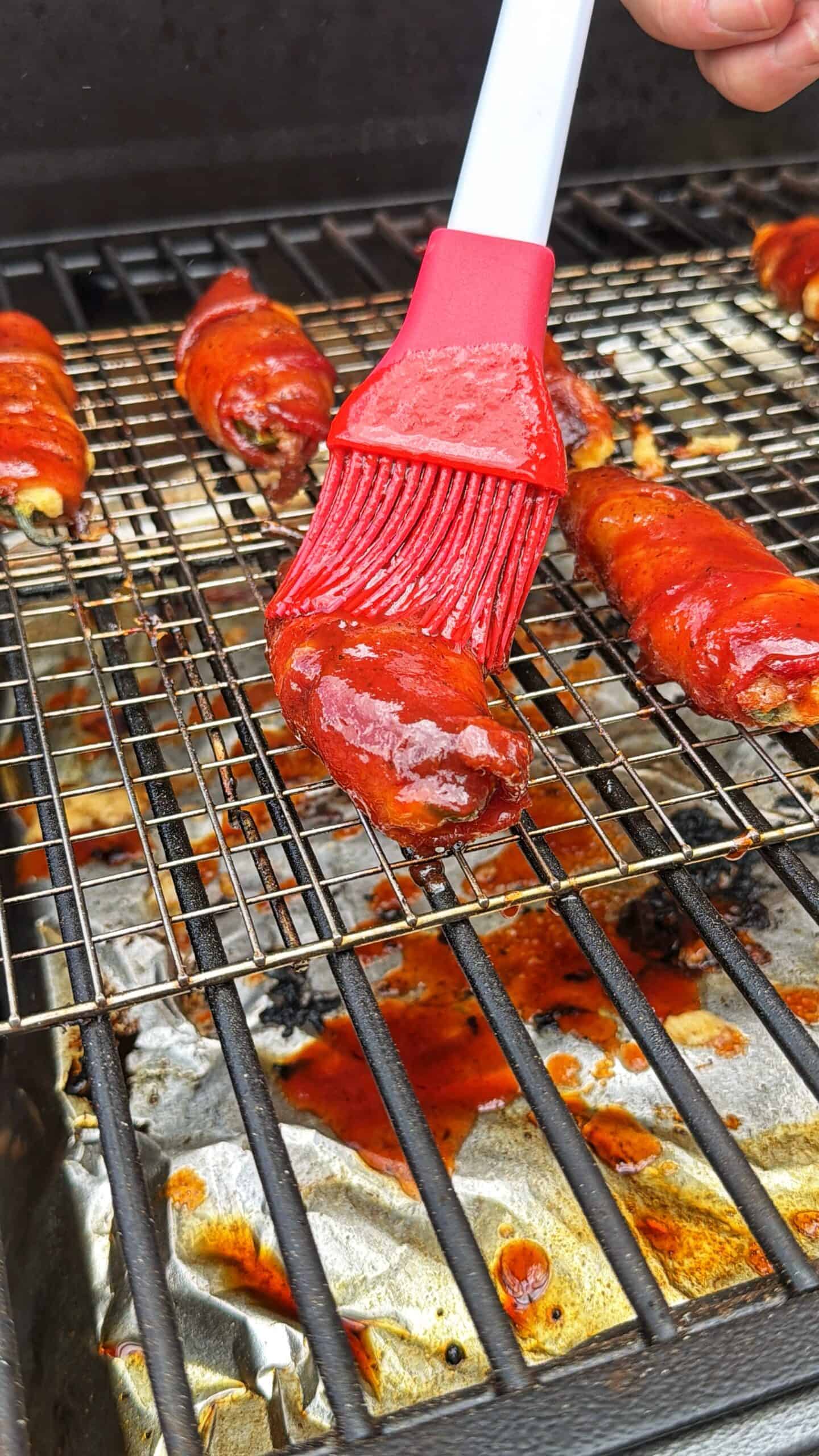 A red brush applies barbecue sauce to meat cooking on a grill. Sauce drips onto foil below the <a href=