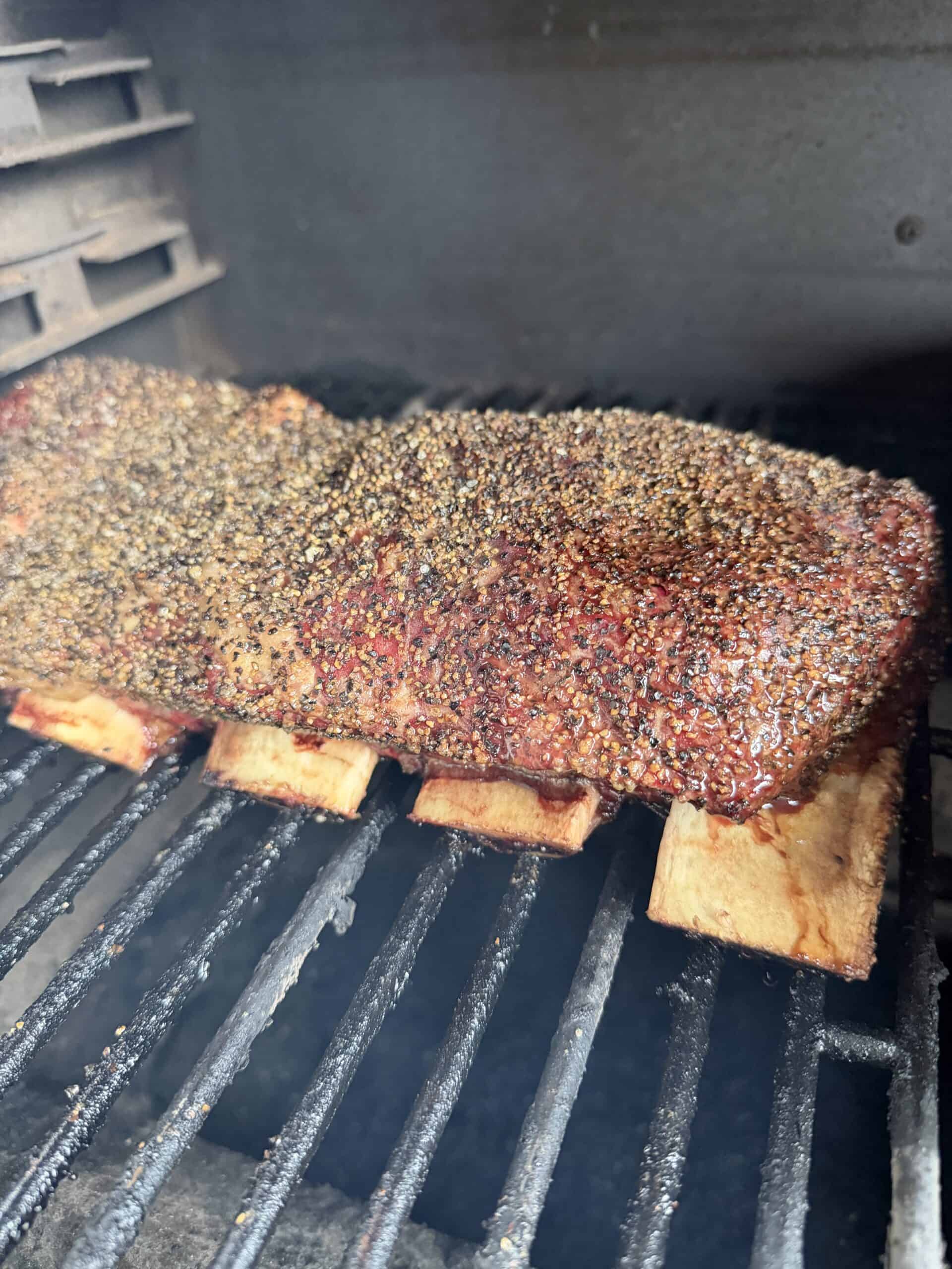 Grill Grates Replacement for Dynaglo DGH450CRP DGH485CRP DGH474CRP Grill on Amazon A close-up of a seasoned slab of meat, likely beef ribs, cooking on a grill inside a smoker, with visible <a href=