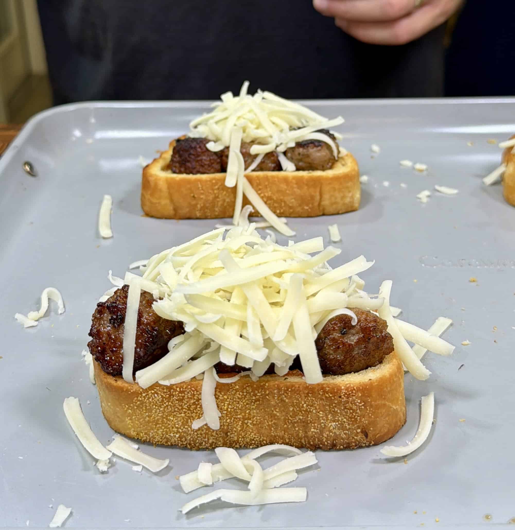 Two slices of bread topped with browned meatballs and shredded cheese sit on a <a href=
