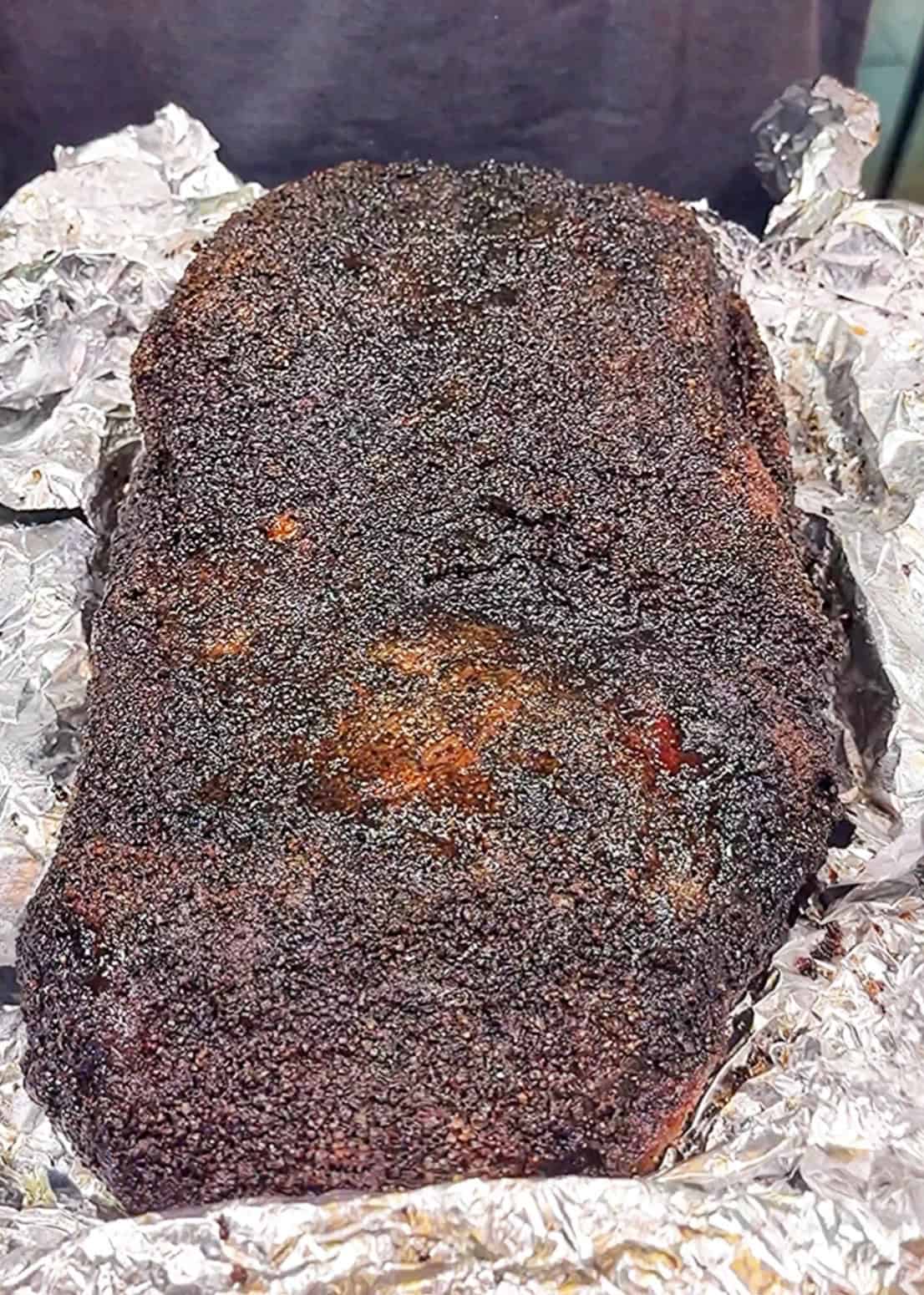 A large smoked brisket with a dark, crispy bark sits on crumpled <a href=