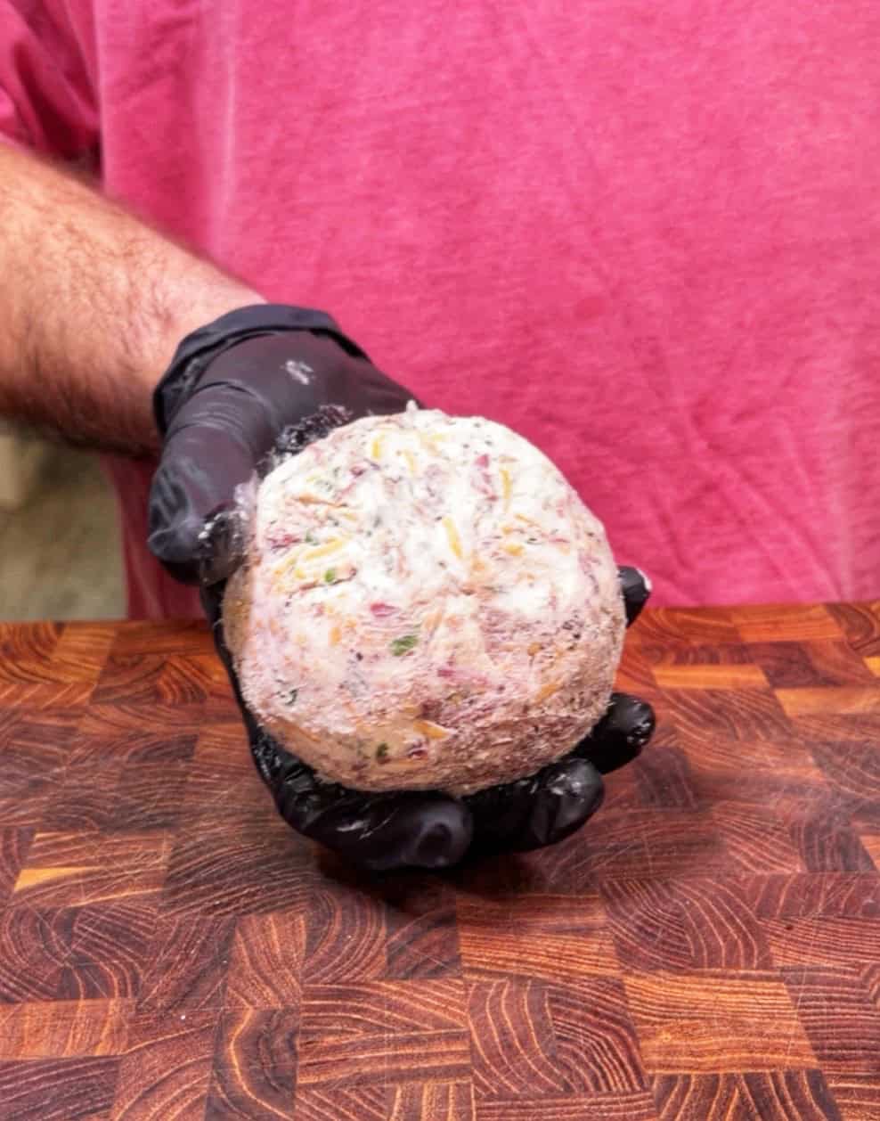 A person in a pink shirt and black glove holds a round, moldy food item over a wooden <a href=