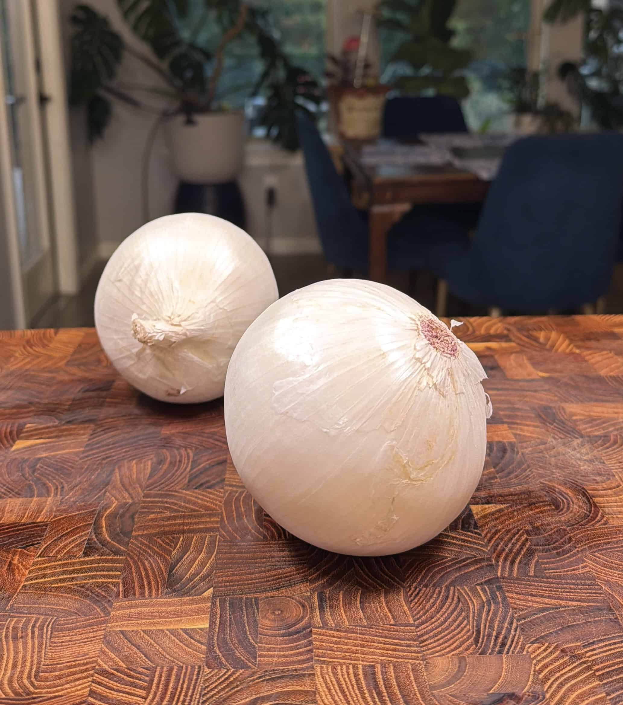 Two whole white onions sit on a wooden <a href=