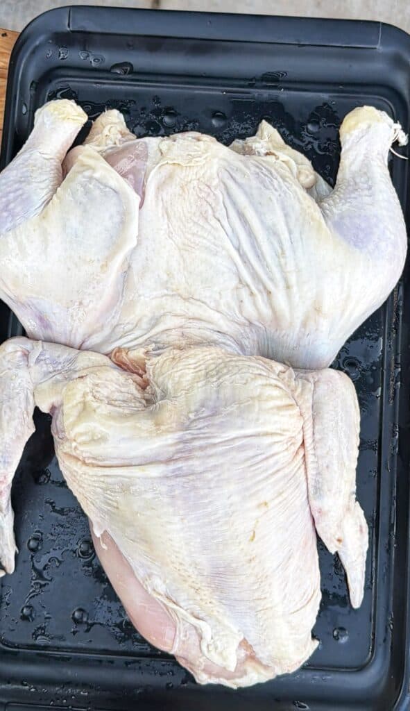 Raw frog-cut chicken laid flat on a black tray.