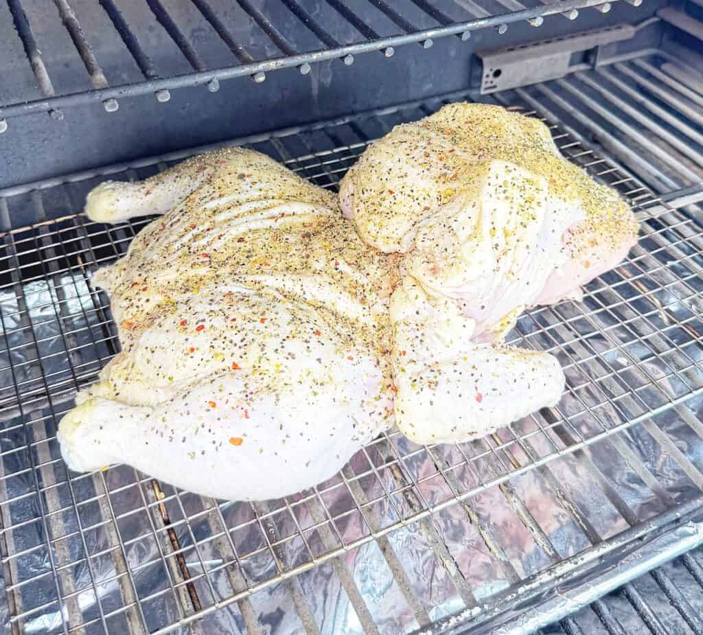 Raw seasoned frog-cut chicken on a wire rack inside a grill.
