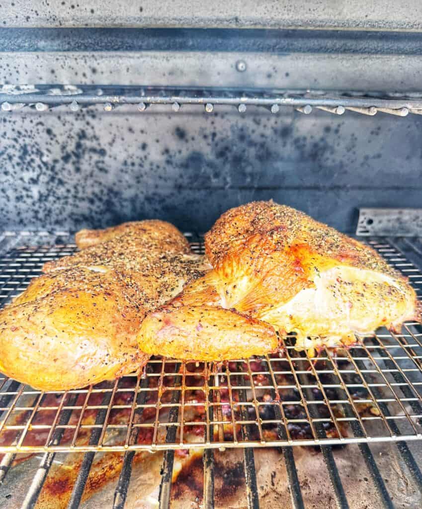 Seasoned frog-cut chicken cooking on a metal rack inside a smoker.