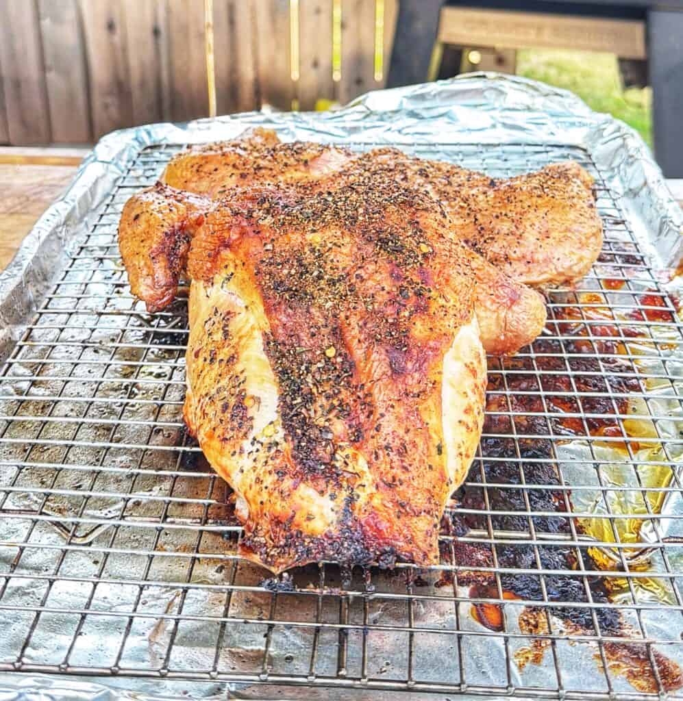 Seasoned frog-cut chicken resting on a wire rack over a foil-lined baking sheet.