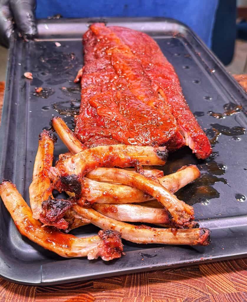 A slab of sauced ribs on a black tray with several removed rib bones in front.