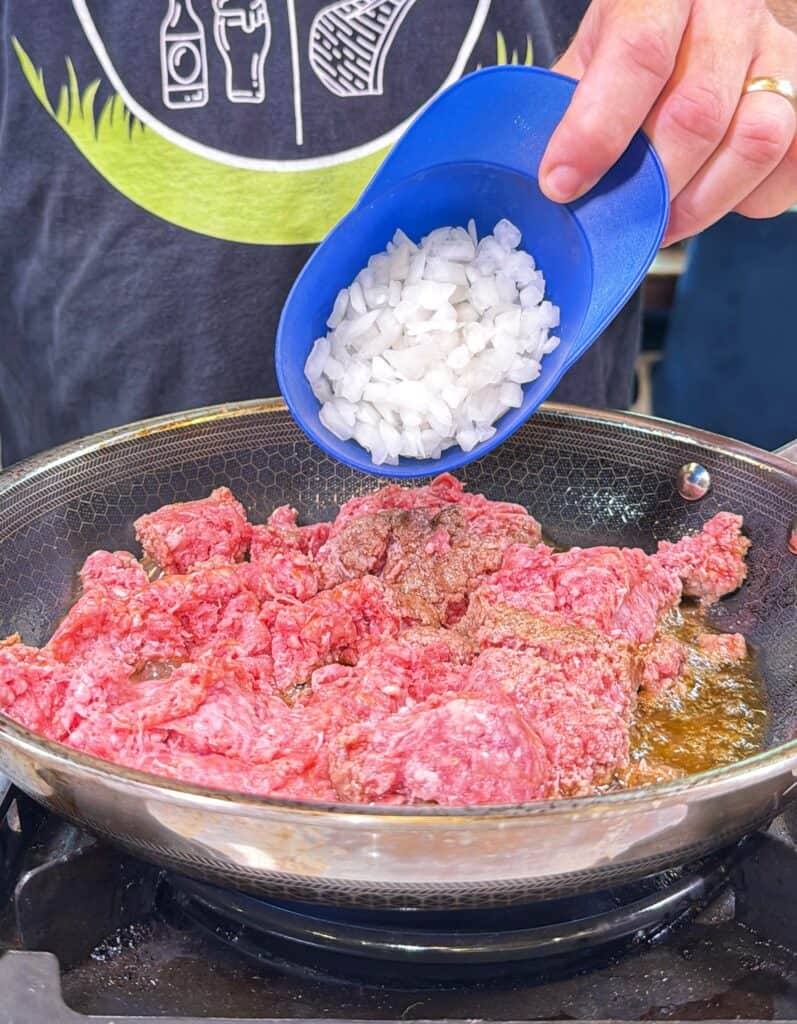 Chopped onion added to ground beef in a frying pan.