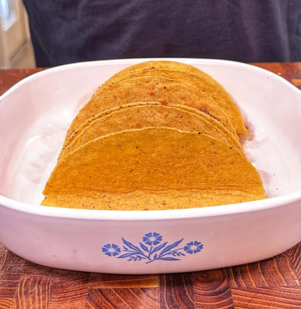 Four hard taco shells standing upright in a baking dish.