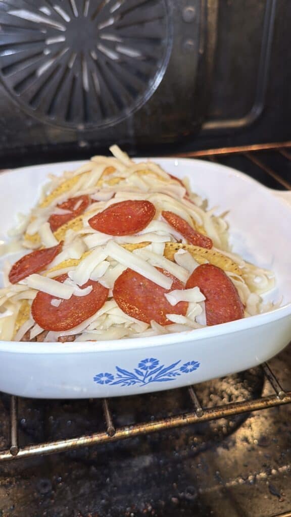 Pizza tacos in a baking dish topped with shredded mozzarella and pepperoni, ready to bake.