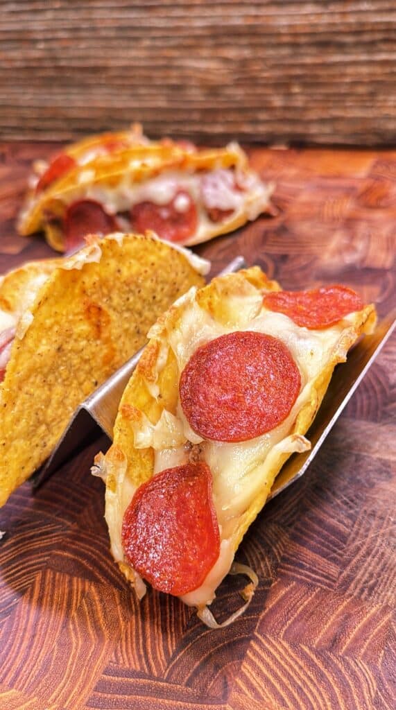 Three pizza tacos filled with melted mozzarella and pepperoni slices in metal taco holders.