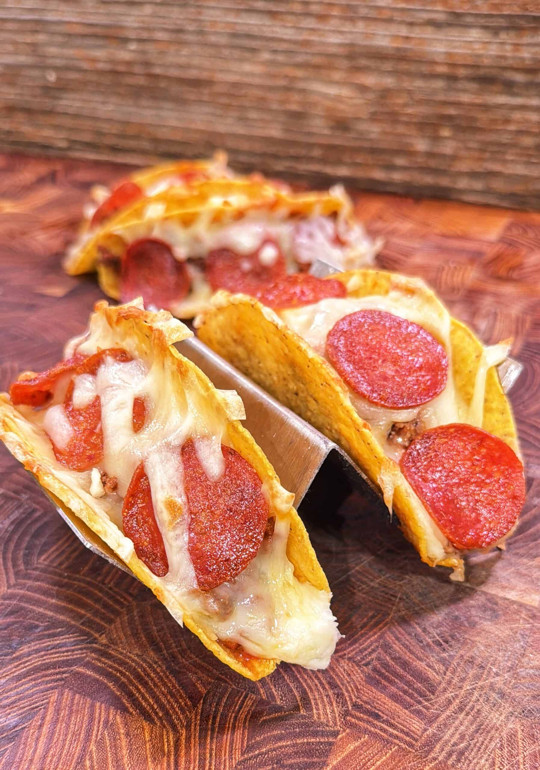 Three pizza tacos filled with melted mozzarella and pepperoni slices in a metal taco holder.