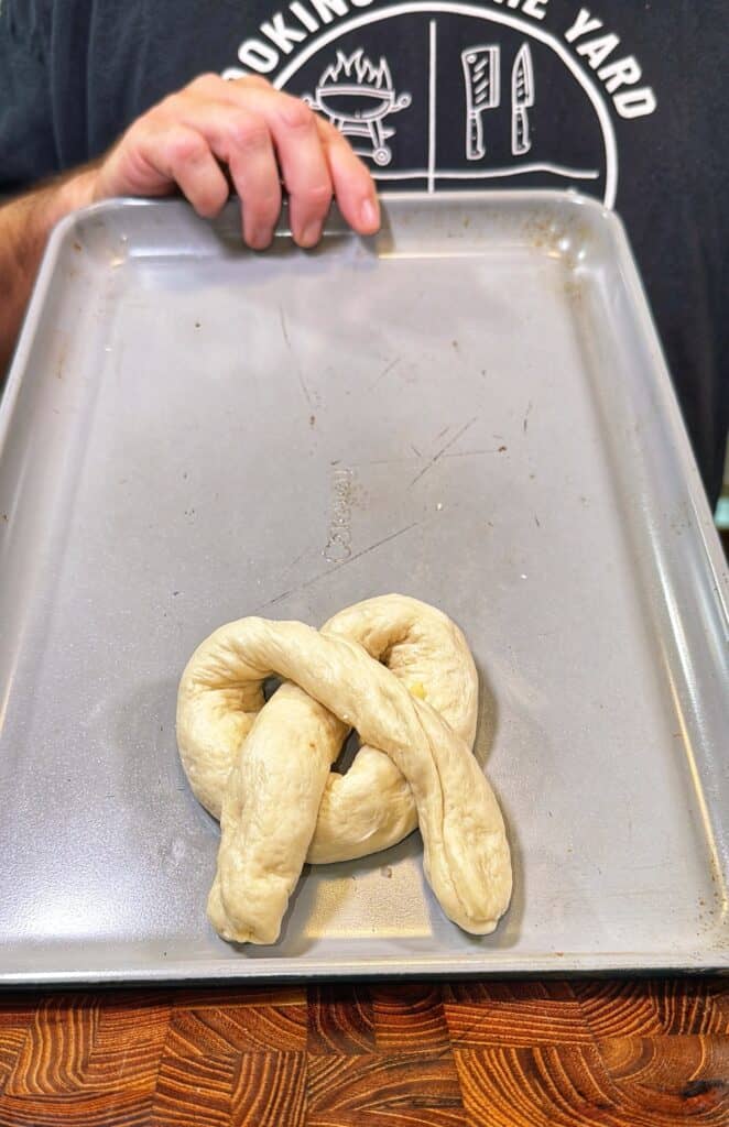 A baking sheet holding an unbaked pretzel-shaped piece of dough ready for baking.