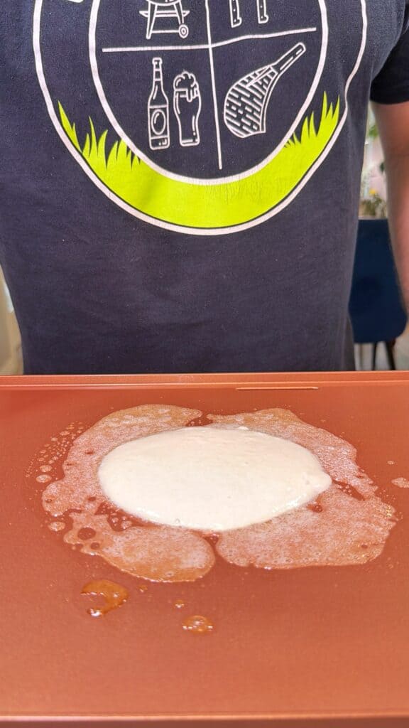 Pancake batter cooks and bubbles on a griddle.