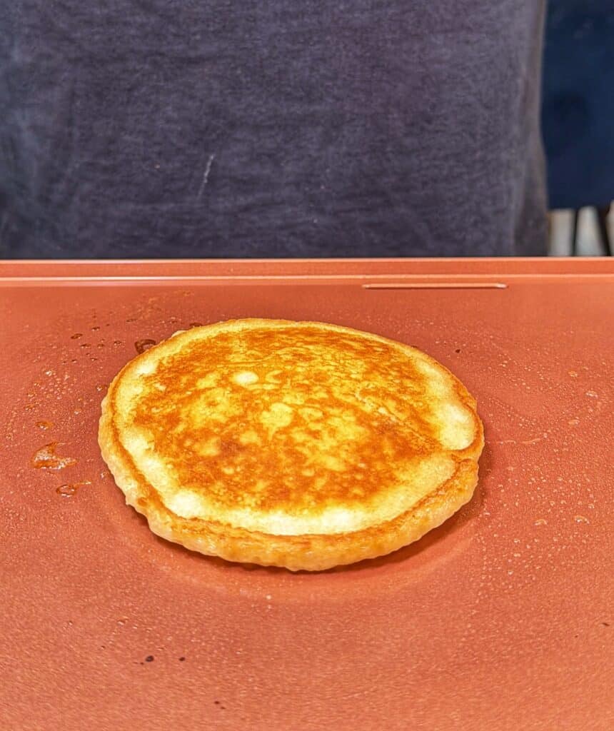 A golden-brown pineapple upside-down pancake cooks on a griddle.