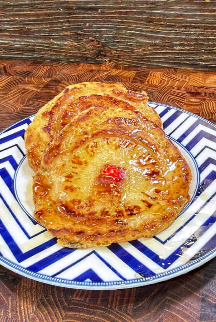 Three glazed pineapple upside-down pancakes with cherries in the centers on a blue and white zigzag-patterned plate.