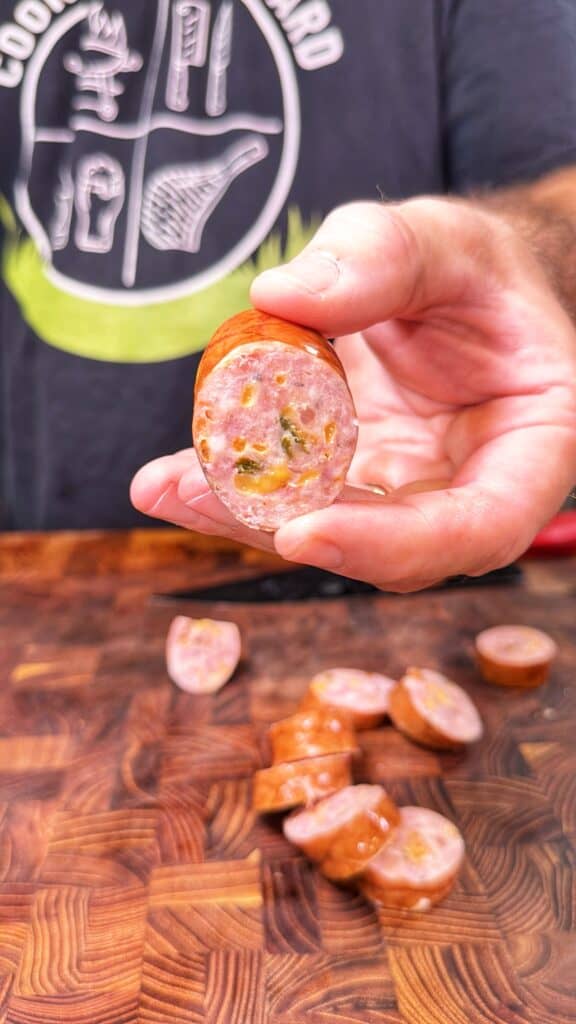 A sliced sausage piece with visible cheese and jalapeño on a wooden cutting board.