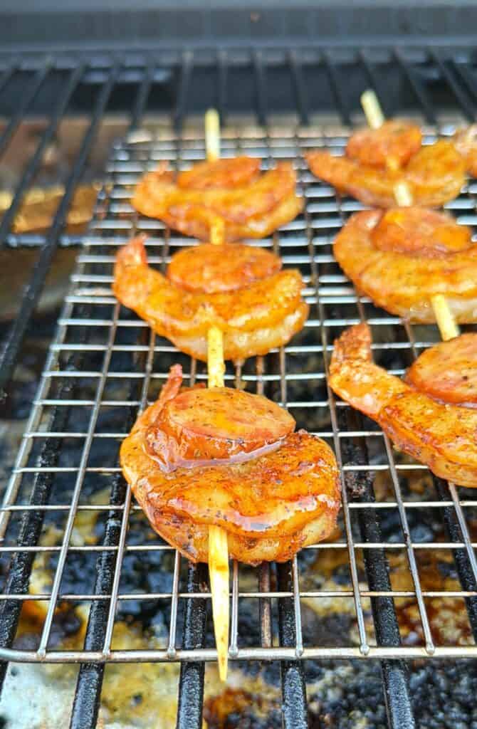 Seasoned shrimp skewers cook on a smoker grate.
