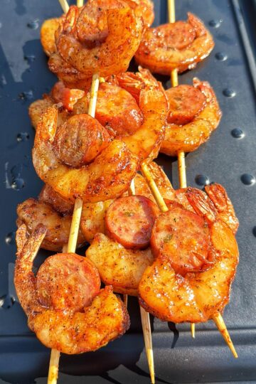 Three shrimp and sausage skewers on a black tray.