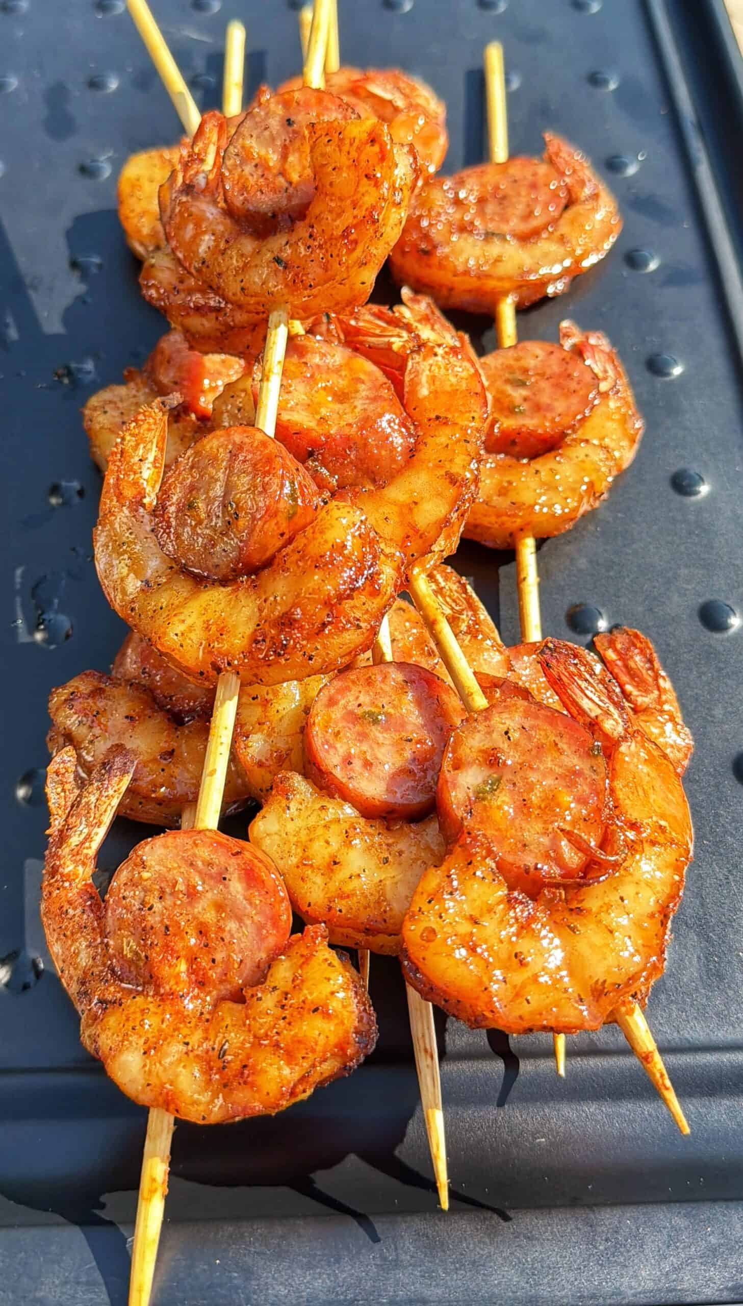 Three shrimp and sausage skewers on a black tray.