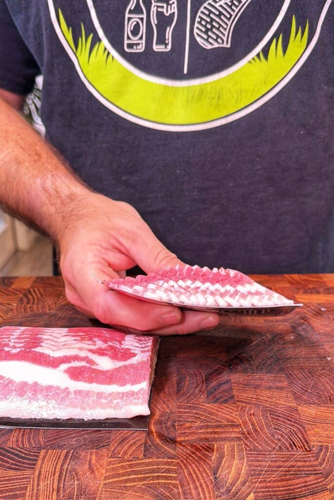 A person slices raw bacon on a wooden cutting board.