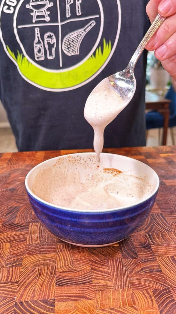 A spoon drips creamy dipping sauce into a blue bowl.