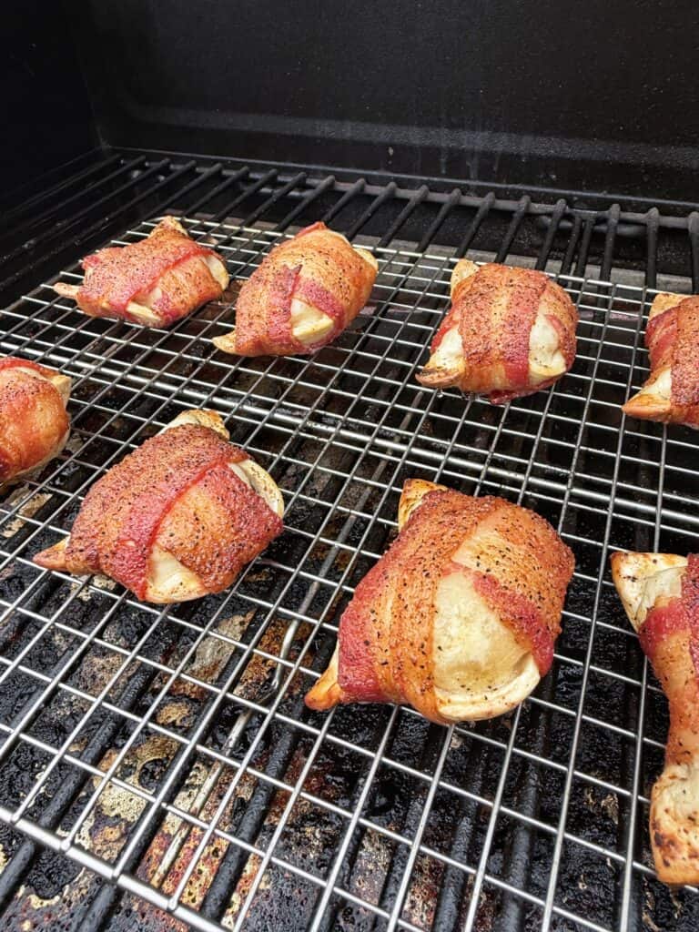 Bacon-wrapped pierogies cook on a wire rack inside a grill or smoker.