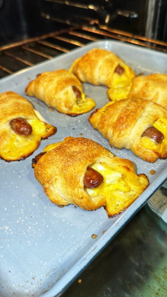Baked sausage, egg, and cheese crescent roll-ups on a baking sheet in an oven.
