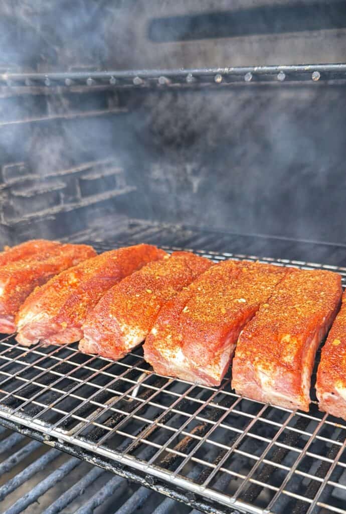 Seasoned individual pork ribs cooking on a smoker rack.