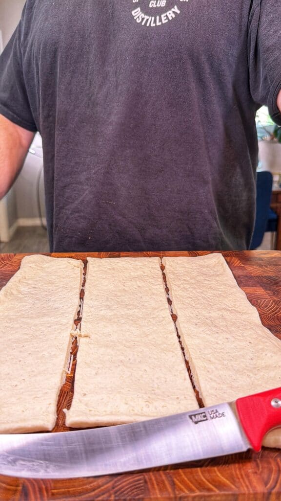 Three strips of pizza dough on a wooden board with a knife.