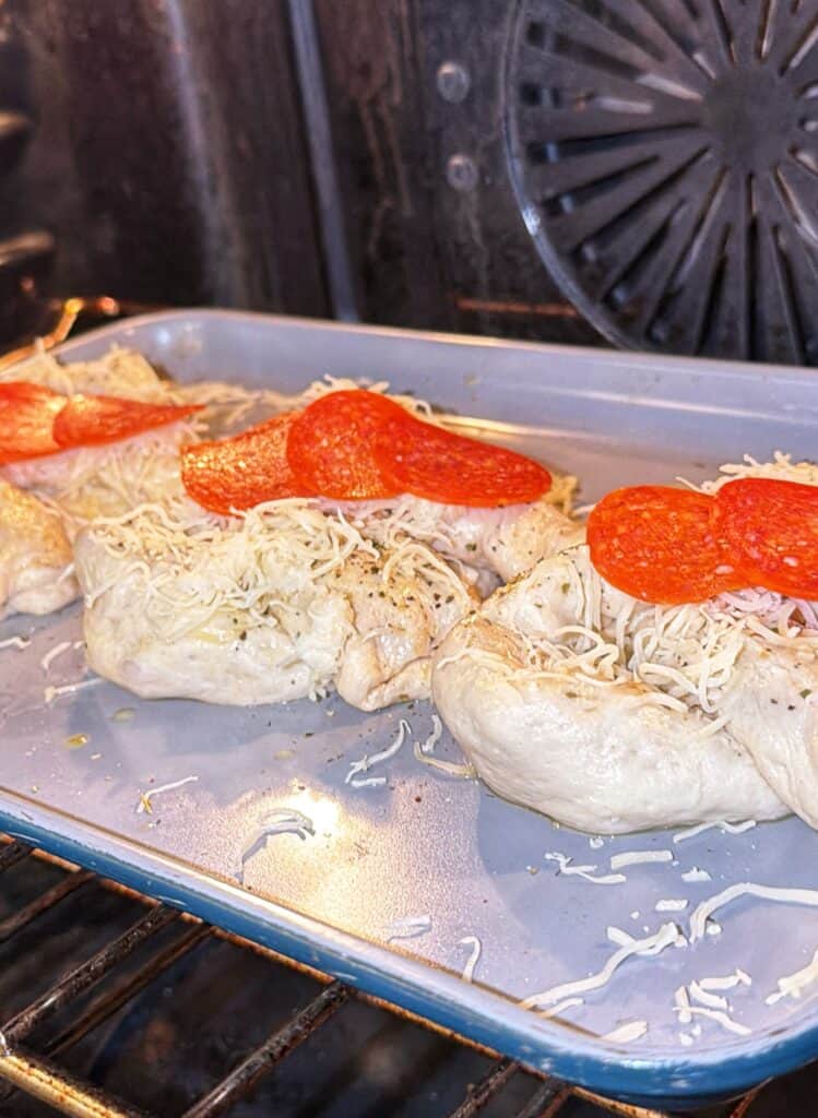 Cheese- and pepperoni-topped stuffed pretzels baking on a tray in the oven.