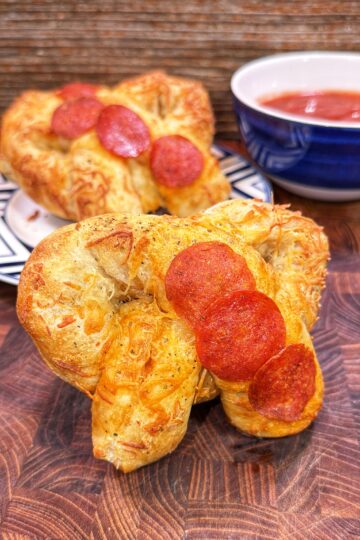 Heart-shaped pepperoni pizza stuffed pretzel with pepperoni slices, with marinara sauce in the background.