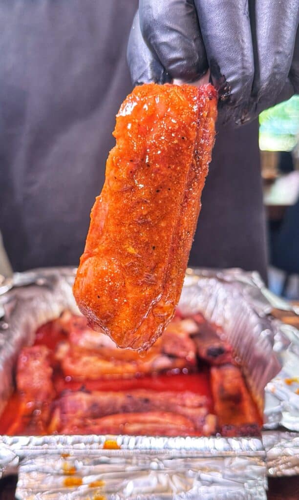 A saucy cooked pork rib held over a foil tray of ribs.