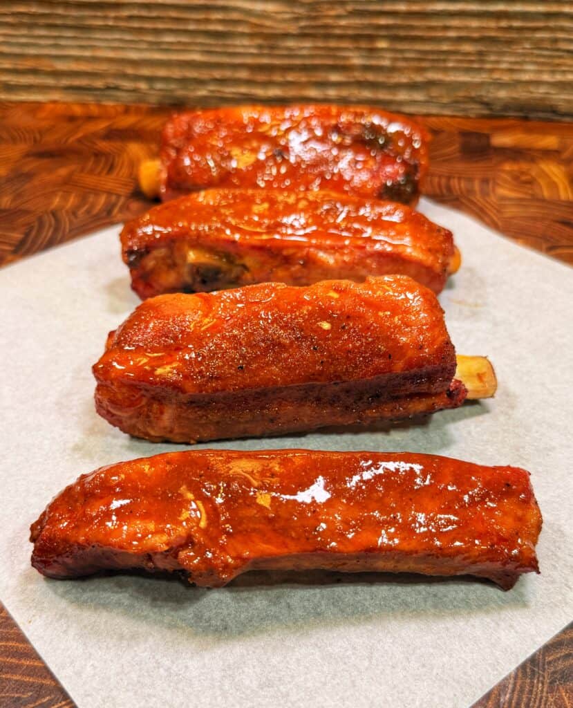 Four glazed pork ribs arranged in a row on parchment paper.