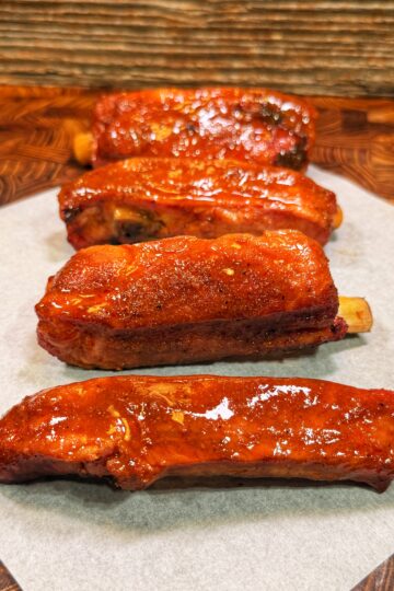 Four glazed pork ribs arranged in a row on parchment paper.