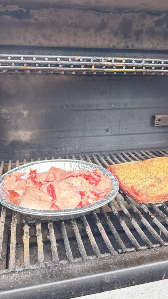 A grill with a tray of sliced beef and seasoned beef ribs cooking on the grates